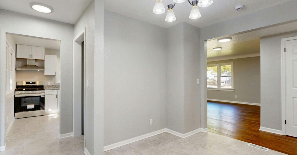 Empty modern home interior showing hallway with kitchen, living room, grey walls and wood flooring lighting