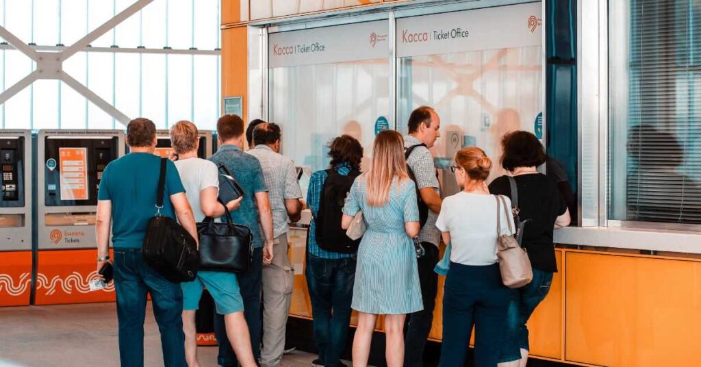 People waiting at a ticket office counter to purchase or collect event tickets before entering a venue.
