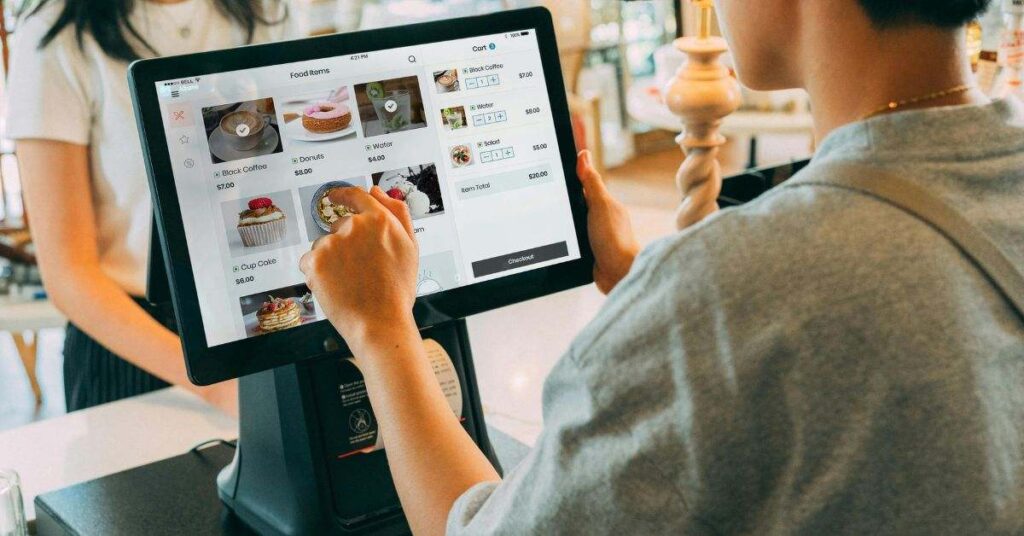 Customer using a touchscreen POS system to browse menu items and complete a digital payment at a café counter.
